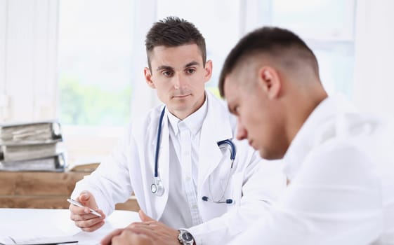 Handsome male medicine doctor with clipboard pad in hands examine patient and prescribe remedy. Exam visitor reception disease prevention ward round visit check 911 healthy lifestyle concept