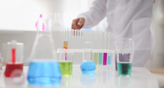 Chemical industry bulb with blue magenta pink liquid lab tubes stand on the table in the laboratory of liquid testing. Test development substances poisons additives stabilizers flavors house cleaning.