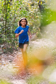 vertical photo of a girl practicing trail running in the forest, concept of sport for children in nature and healthy lifestyle, copy space for text