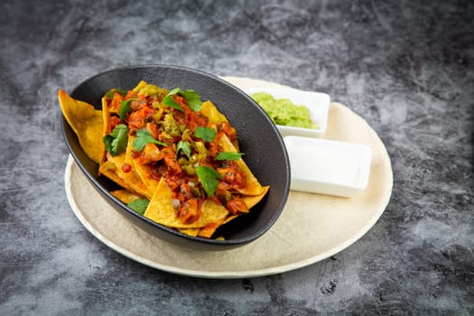 nachos with sauce, meat and herbs in a black plate