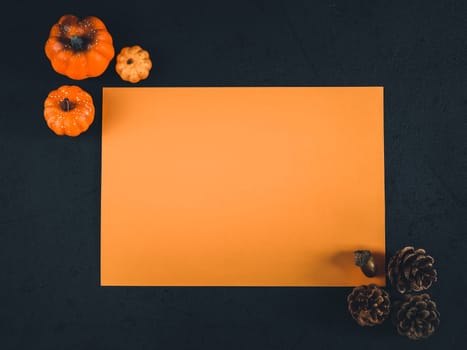 One orange empty leaf lie horizontally in the middle on a black background with decorative pumpkins and pine cones on the sides. Flat lay close up.