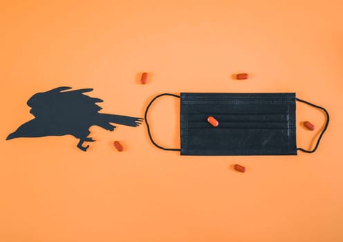 BlacBlack medical mask, red pills and paper crow lie in the middle on an ornamental background with space for text on the sides, flat lay close-up. Scary concept and coronavirus.k medical mask, pills and paper crow.