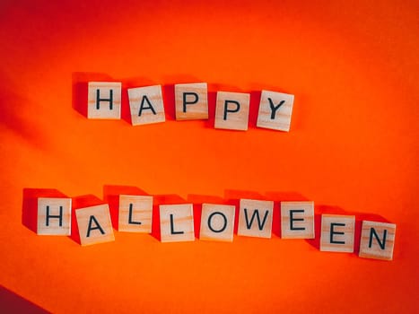 Wooden cubes with the inscription happy halloween lie in the middle on a red-orange background, flat lay close-up.Magic concept greeting card.