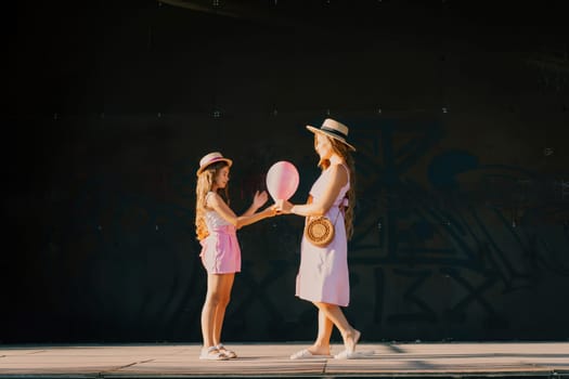 mother and daughter stand in pink dresses with flowing long hair on a black background. Enjoy communicating with each other.