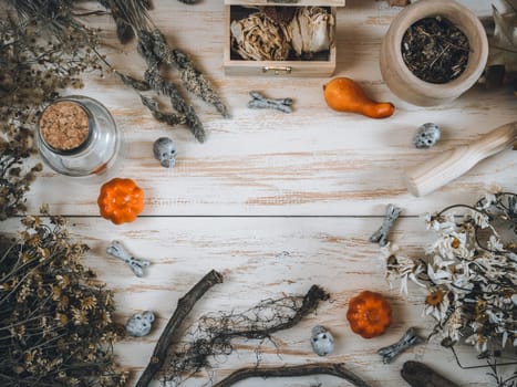 Dry herbs, three pumpkins, jar, mortar, chest, decorative scoops and bones lie in a round frame on a wooden table with space for text in the center, top view close-up. Concept of making a potion for halloween.