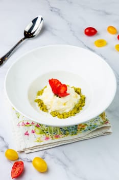 curd dessert with strawberries on top in a white plate on a marble background