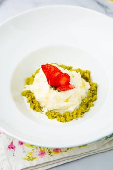 curd dessert with strawberries on top in a white plate on a marble background