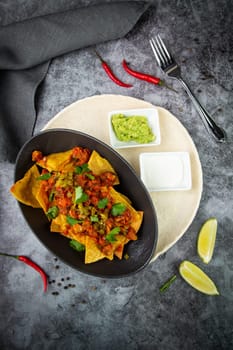 nachos with sauce, meat and herbs in a black plate