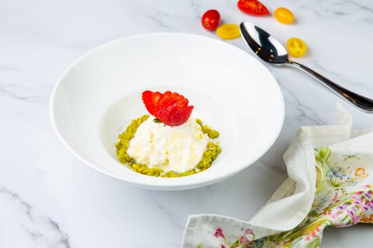 curd dessert with strawberries on top in a white plate on a marble background