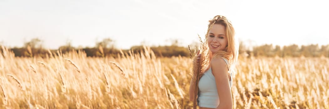 Beautiful blonde woman on a walk in a field with dry grass. A walk in nature, sunset in a field of pampas grass. Life style.