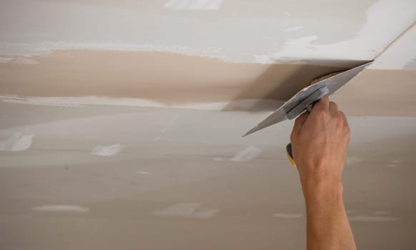 A man puts putty on a plasterboard ceiling. Putty for the joints of plasterboard sheets. Selective focus