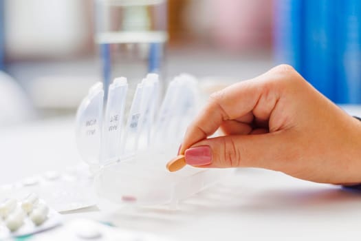 Woman hand putting pills into open pill organizer or plastic pillbox. Sorting of tablets for daily use according to a doctor's prescription