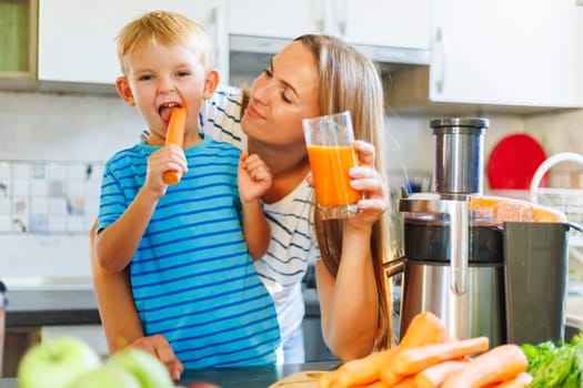 Mom and son drink fresh carrot juice squeezed using a juicer in the kitchen at home. Family nutrition, healthy eating concept