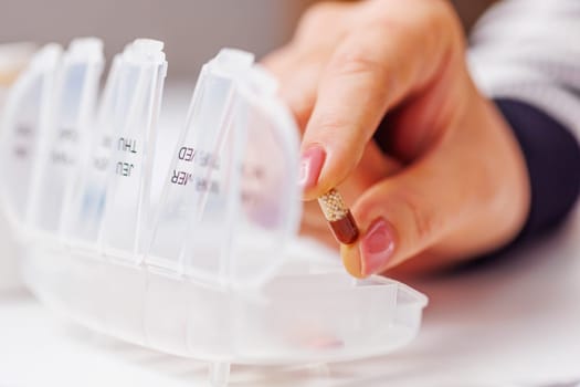 Woman hand putting pills into open pill organizer or plastic pillbox. Sorting of tablets for daily use according to a doctor's prescription