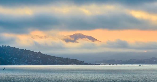 Image of Golden sunset behind misty cloud shrouded mountain on aerial across San Francisco Bay water