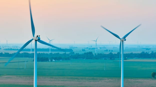 Image of Wind turbines caught in motion on hazy morning with soft pink sky aerial