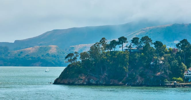 Image of Hazy peninsula on ocean with fancy house on cliff and docks below and mountain behind aerial