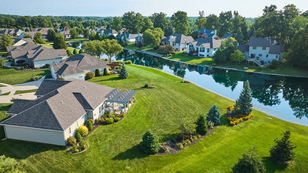 Image of Low aerial over neighborhood houses with pond view and landscaping