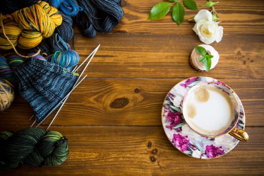 Colored threads, knitting needles and other items for hand knitting, on a dark wooden table .