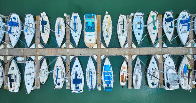 Image of Variety of boats and yachts docked at pier in aerial straight down shot of teal ocean water