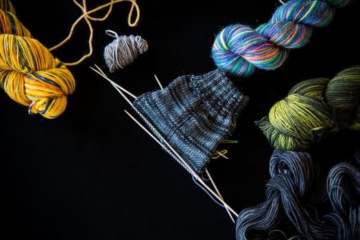 Colored threads, knitting needles and other items for hand knitting, on a black background .