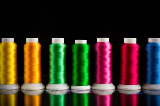 set of different color sewing threads, isolated on black background.