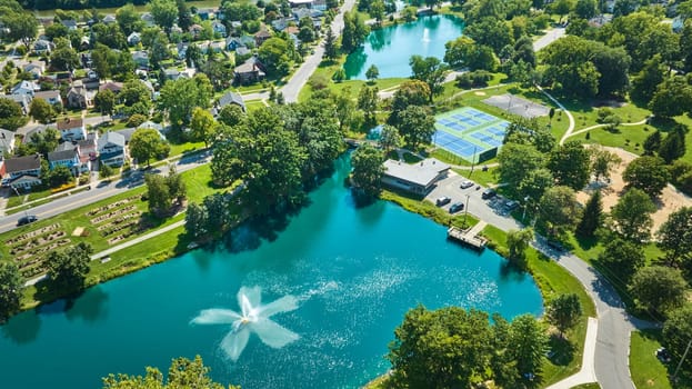Image of Aerial over Lakeside Pond with fountain near playground and tennis courts in neighborhood