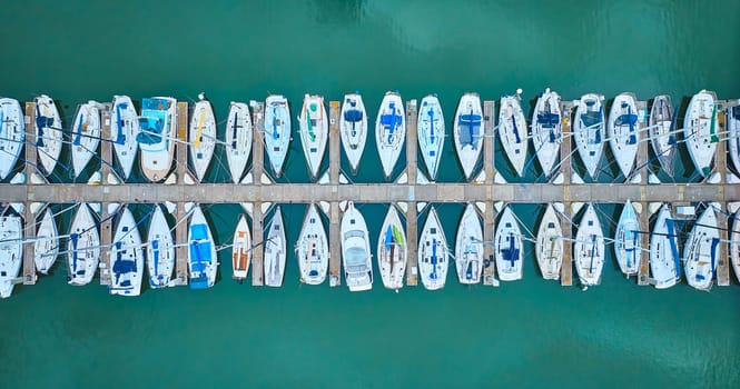 Image of Aerial straight down view perfect row of boats on pier dock area with teal ocean water