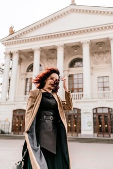 Woman street lifestyle. Image of stylish woman walking through European city on sunny day. Pretty woman with dark flowing hair, dressed in a beige raincoat and black, walks along the building