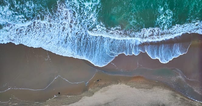 Image of Straight down aerial of tan beach with green ocean waves at top washing over wet sand