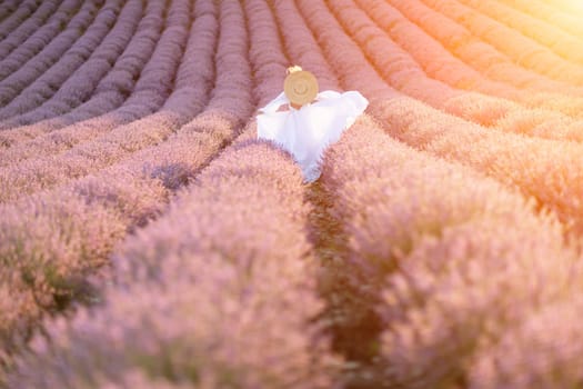 Happy woman in a white dress and straw hat strolling through a lavender field at sunrise, taking in the tranquil atmosphere