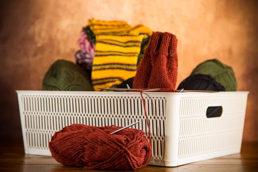 Colored yarn, knitting needles and other items for hand knitting in a box on a dark wooden table.