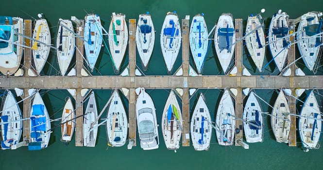 Image of Aerial straight down close up view row of boats on pier dock area with teal ocean water