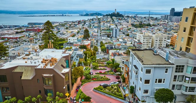 Image of Winding Lombard Street with cars going downhill with distant Coit Tower aerial