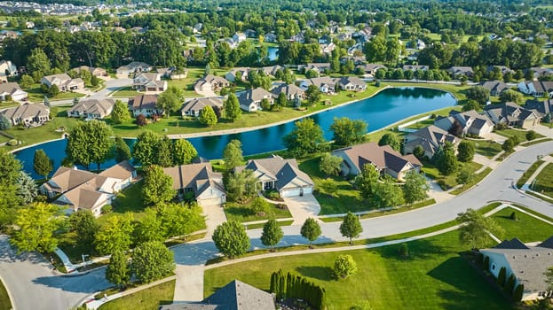 Image of Sunny day over suburban neighborhood with long manmade pond between houses aerial