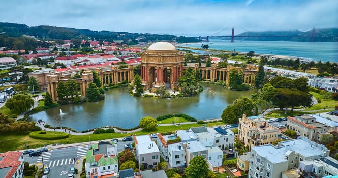 Image of Palace of Fine Arts colonnade and open rotunda on pond with city and Golden Gate Bridge aerial