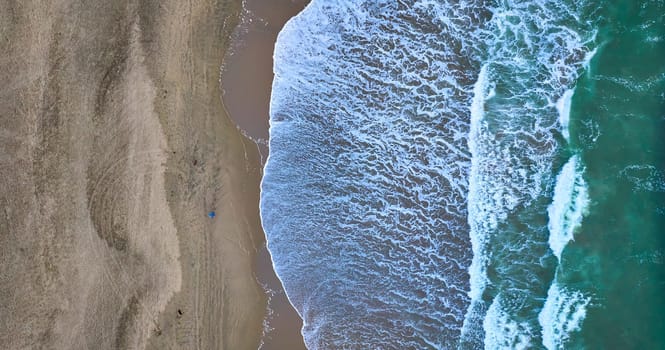 Image of Downward wide aerial of green ocean waves on right with wet sandy beach on left