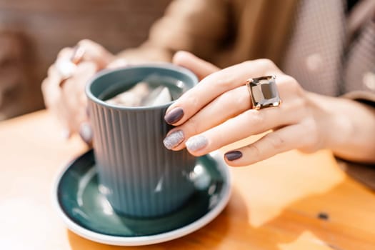 woman holding a cup of hot cappuccino coffee in a cafe on the street, rings on her fingers