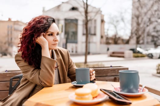 stylish woman in a beige coat drinks coffee outdoors in a cafe