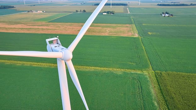 Image of Sunset golden hour lighting on wind turbine blades in lush green field aerial