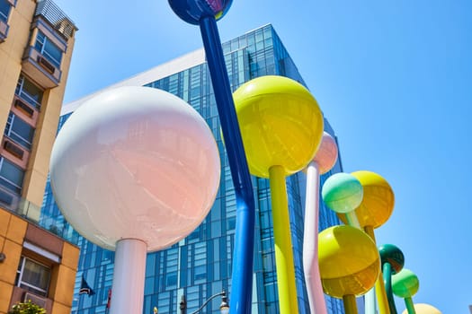 Image of Assorted colored balls on tall twisted poles abstract sculpture with San Francisco skyscraper behind