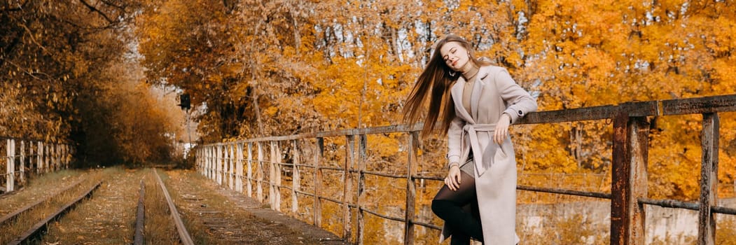 A beautiful long-haired woman walks through the autumn streets. Railway, autumn leaves, a woman in a light coat.