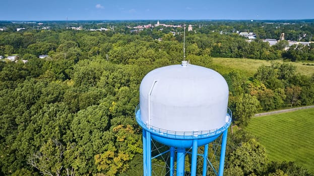 Image of Generic backside of water tower close up with white top and blue base aerial distant city