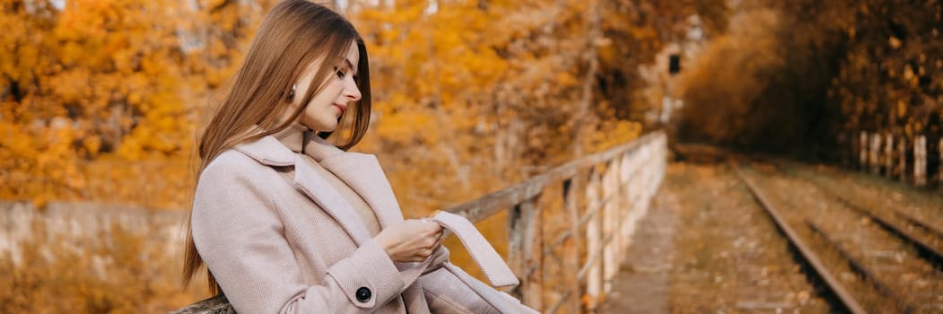 A beautiful long-haired woman walks through the autumn streets. Railway, autumn leaves, a woman in a light coat.