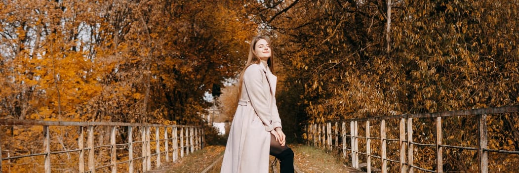 A beautiful long-haired woman walks through the autumn streets. Railway, autumn leaves, a woman in a light coat.