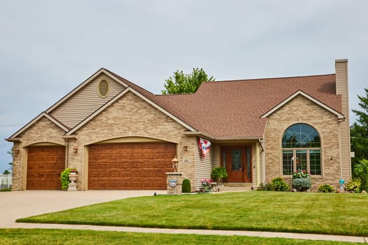 Image of Brown house with bricks on front and brown wooden door and garage doors with large front window