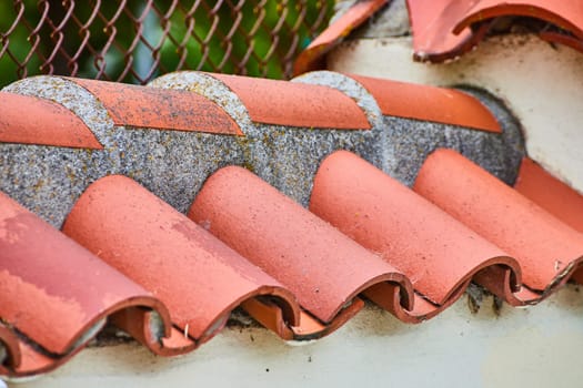 Image of Orangish red roof shingles along wall with dirty tiles overhanging a white wall close up view