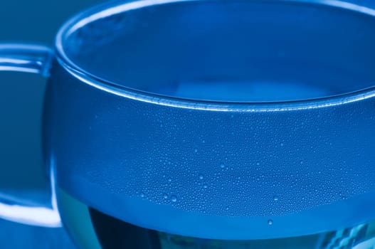 Detail of a glass cup with white tea and drops of condensation in blue tint