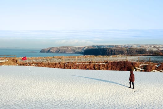 child on a snow covered golf course in ireland in winter with sea and cliffs in background