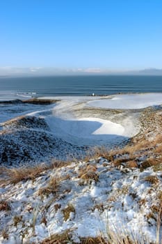 snow covered links golf course in ireland in winter with sea background
